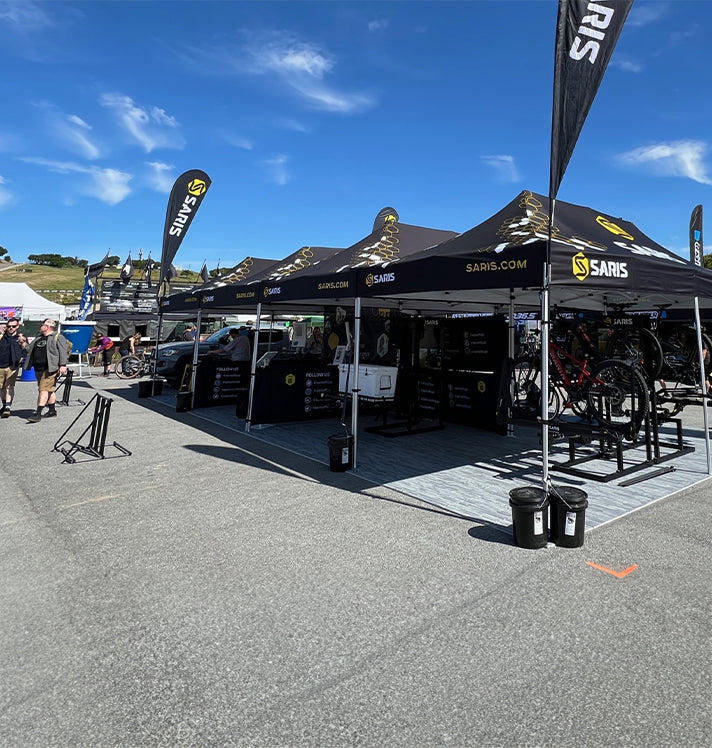 Saris branded expo booth at Sea Otter Classic — portrait crop showing black tents, Saris feather flags, and display bikes