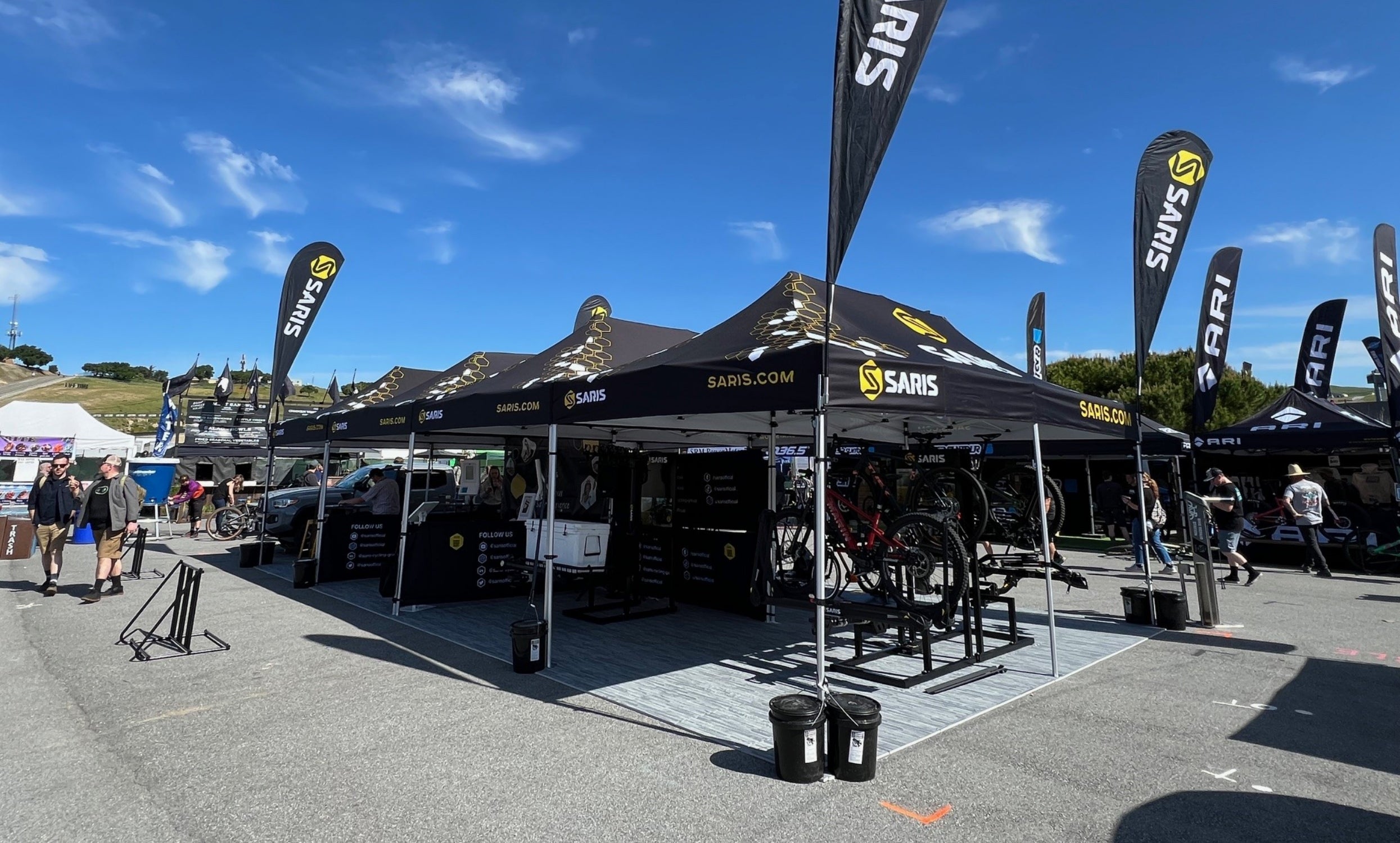 Saris branded expo booth at Sea Otter Classic — black tents with Saris logos and feather flags, bikes on display racks