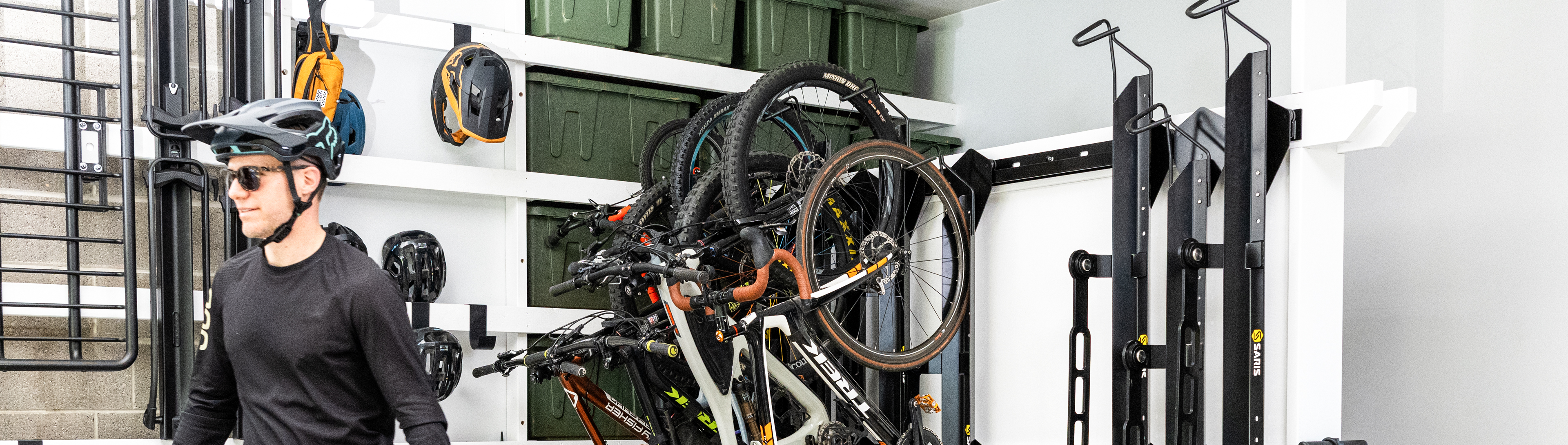 Cyclist with helmet beside Saris Cycle Glide wall-mounted storage system holding multiple mountain bikes in a garage